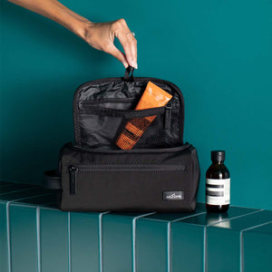 black travel kit with open top featuring some grooming products visible from the inside pockets.