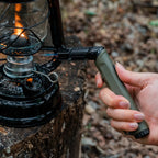 Olive green outdoor ignition tool held beside camping gear